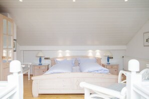 A bedroom with a bed, two bedside tables, a nightstand, and a window. - Beach Villa Atlantic App. 03 (Norderney)
