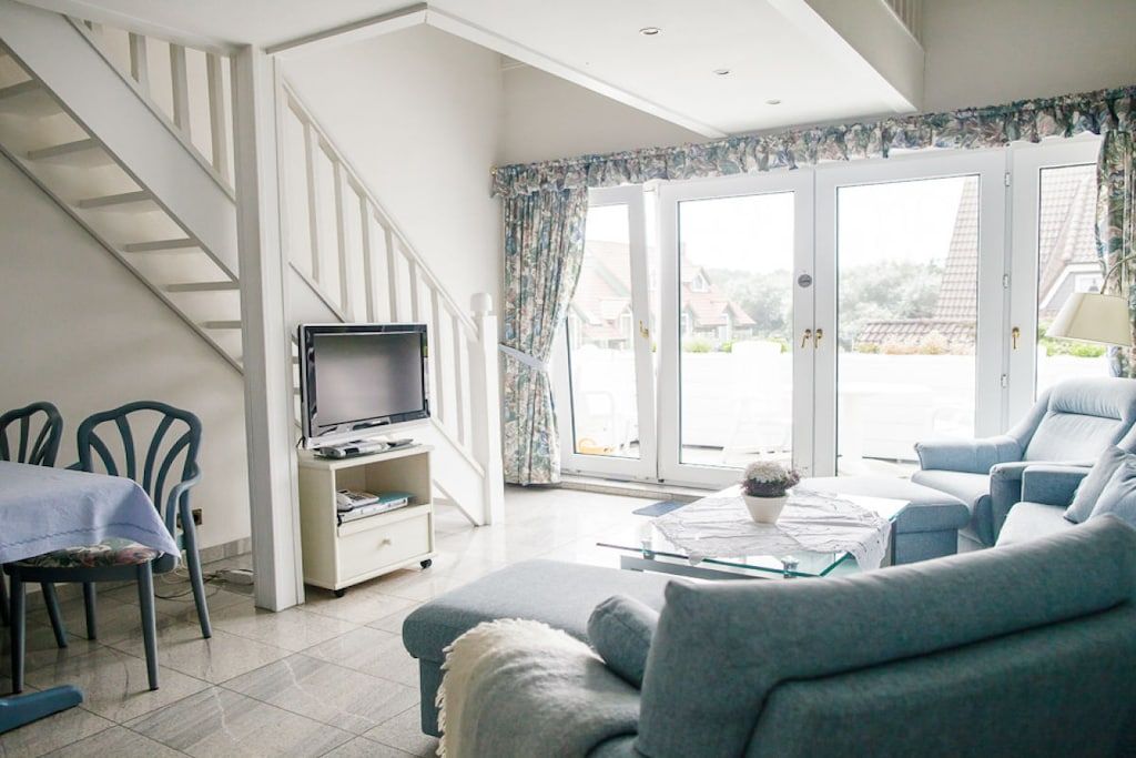 A living room with a sofa, a television, a dining area with chairs, and a staircase.
