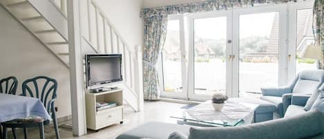 A living room with a sofa, a television, a dining area with chairs, and a staircase.