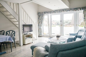 A living room with a sofa, a television, a dining area with chairs, and a staircase. - Beach Villa Atlantic App. 03 (Norderney)