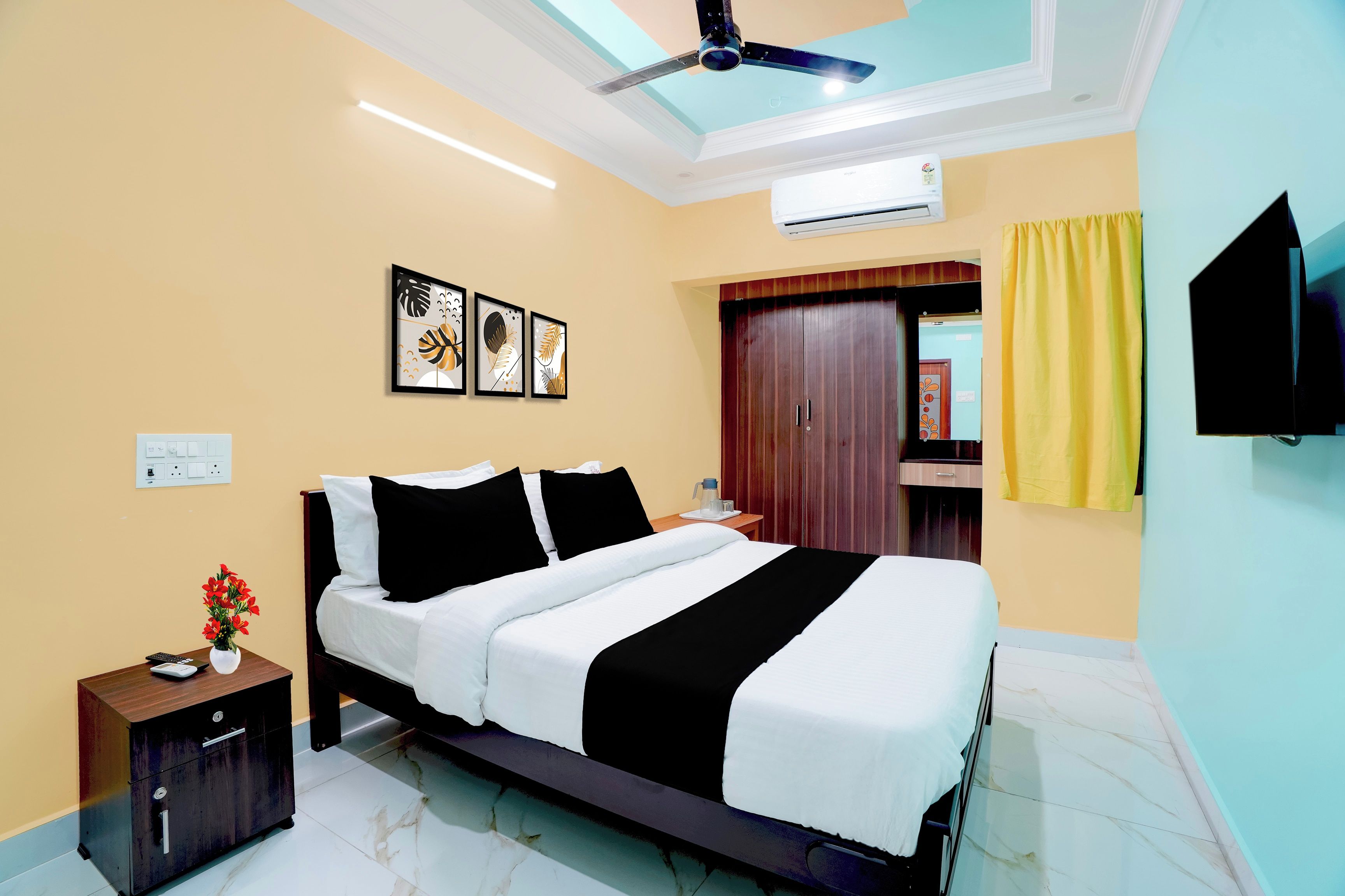 Quarto de hotel com cama, mesa de cabeceira, obras de arte, guarda-roupa e ventilador de teto.