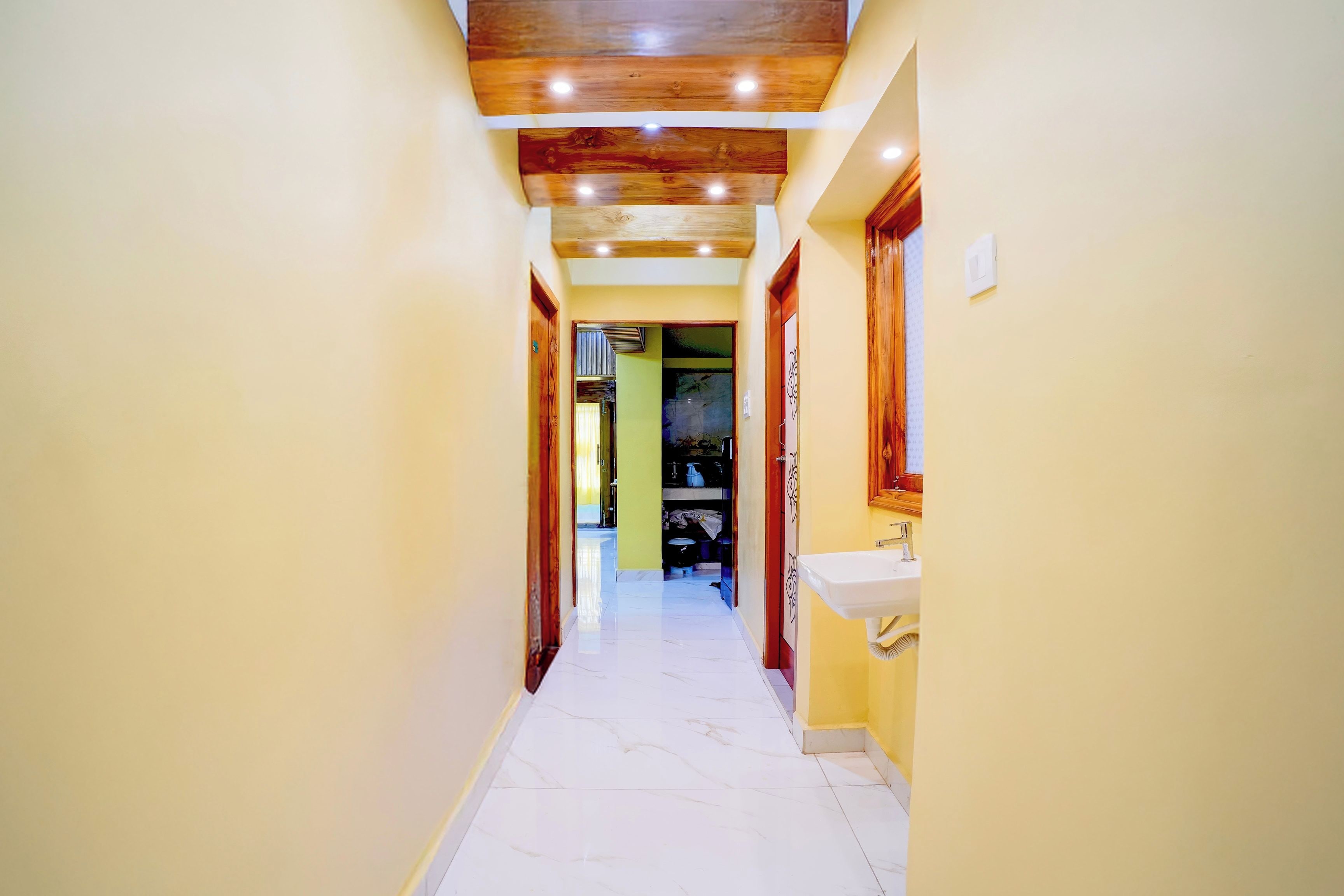 Un pasillo con techo de madera, piso de baldosas blancas y pared amarilla.