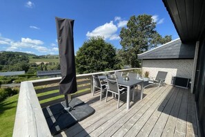 Um terraço com móveis para área externa, churrasqueira e vista para o campo.