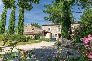 A stone building with a sloped roof, surrounded by greenery and trees. - Gite Louise - Mas Paraloup (Lagorce)