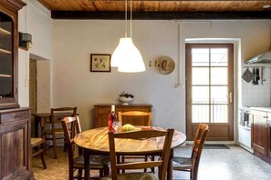 A dining area with a round wooden table, chairs, a hanging pendant light, and a window with a view of the outside. - Gite Louise - Mas Paraloup (Lagorce)