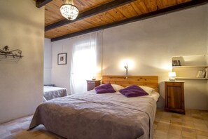 A bedroom with a large bed, two bedside tables, a wooden ceiling, and a wall-mounted shelf with books. - Gite Louise - Mas Paraloup (Lagorce)