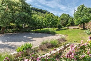 A gravel driveway leading to a grassy area with trees and a stone structure. - Gite Louise - Mas Paraloup (Lagorce)