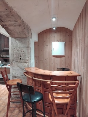 A rustic kitchen with a wooden bar, two chairs, and a television mounted on the wall. - La Tour Au Comté Vacation Rental. Experience the authentic lifestyle, from a 15th-century tower to farm life. (Charency)