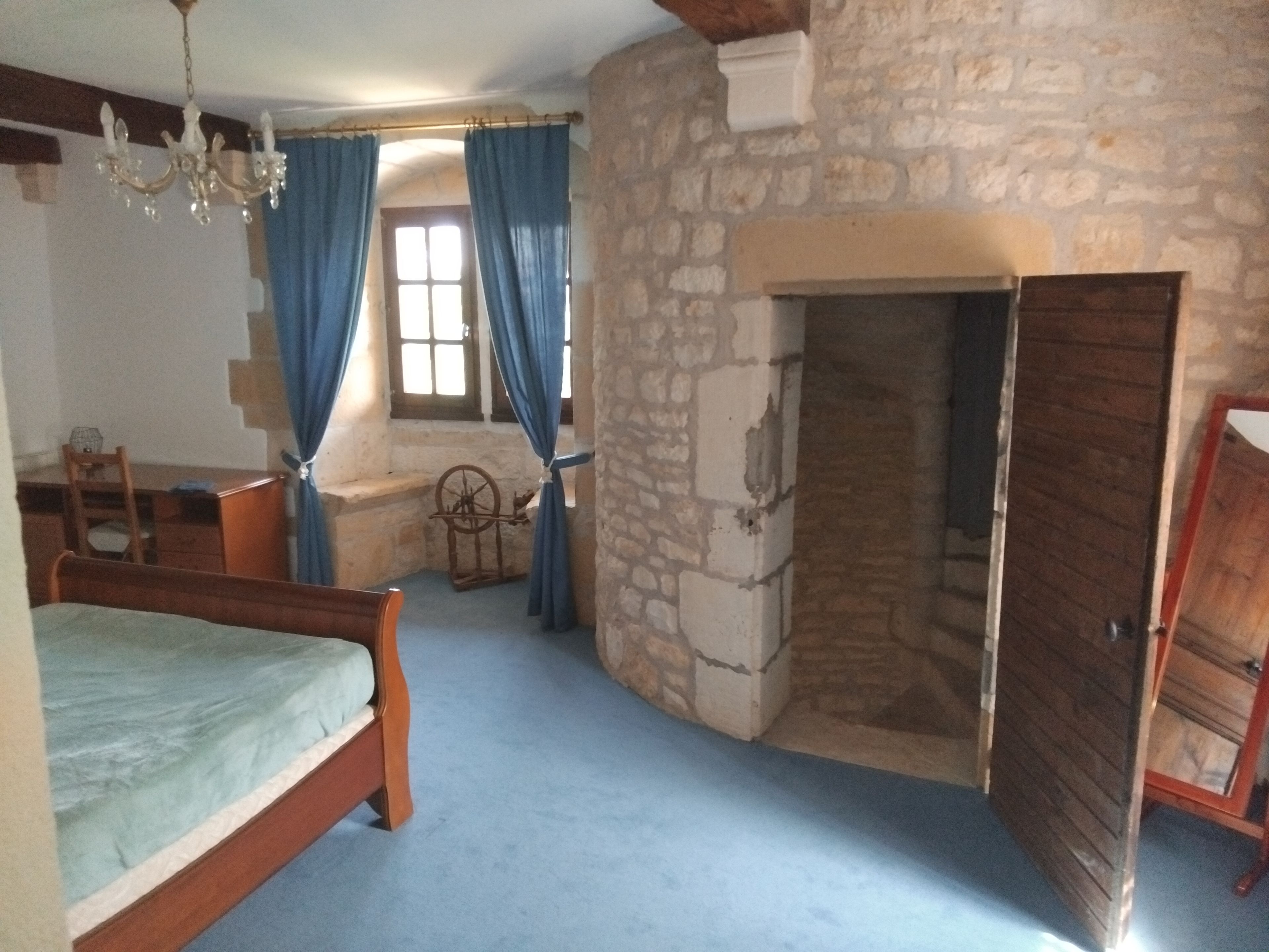 Un dormitorio con pared de piedra, cama de madera, escritorio, silla y candelabro.