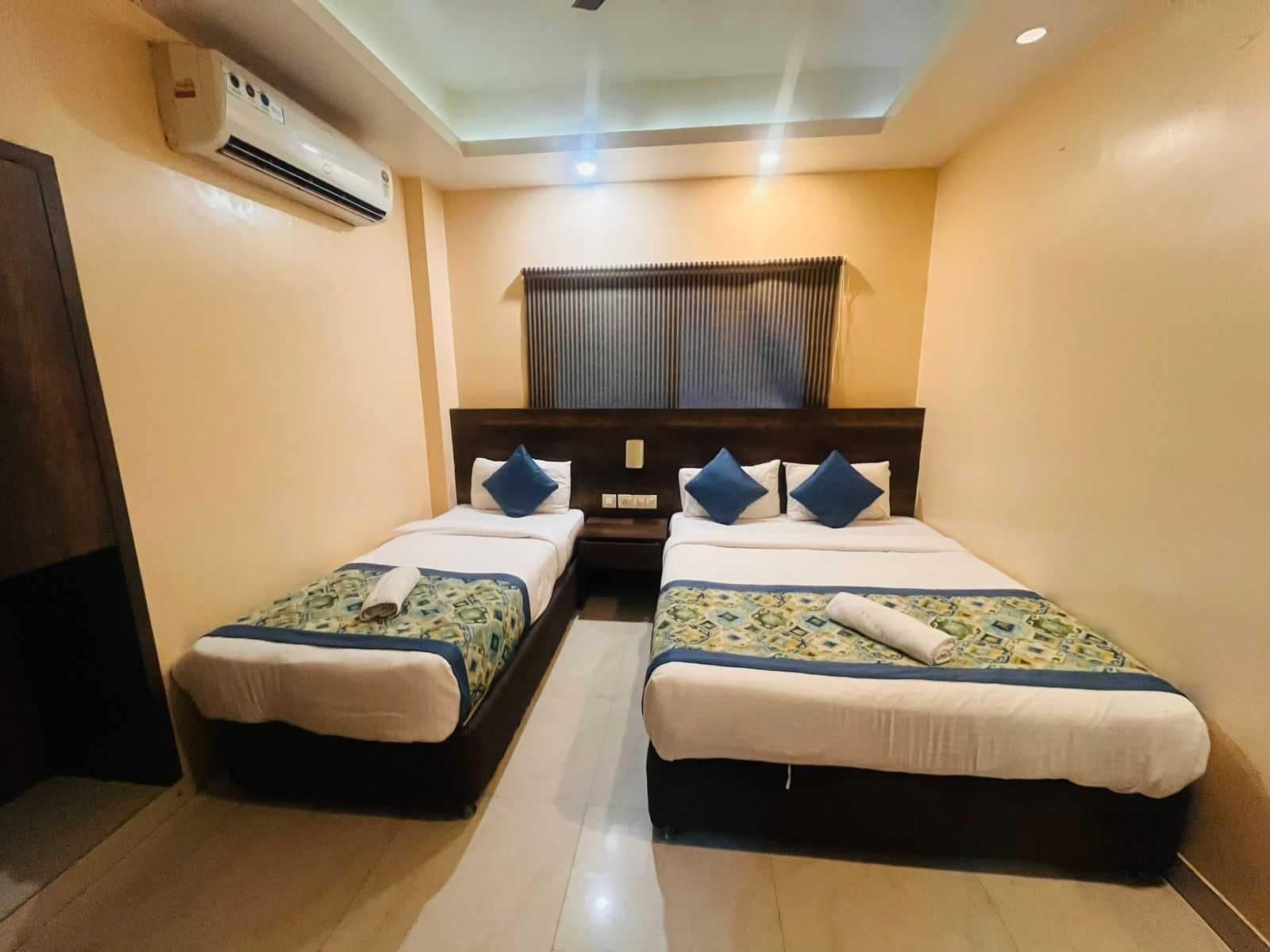 Habitación de hotel con dos camas, ventilador de techo, aire acondicionado y una ventana con persianas.