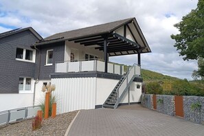 A modern two-story house with a covered patio, a staircase, and a view of a hilly landscape. - Holiday apartment with 1 bedroom (Schmallenberg-Grafschaft)