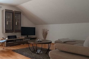 A modern living room with a flat-screen TV, a sofa, a coffee table, and built-in shelving. - Holiday apartment with 1 bedroom (Schmallenberg-Grafschaft)