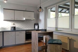 Una cuina moderna amb armaris grisos, una taula de fusta i una finestra amb persianes.