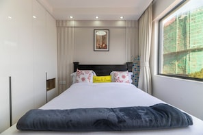 A modern hotel room with a large bed, a window with a view of construction, and a framed picture on the wall. - Cozy 2-bedroom apartment in beautiful Westlands Nairobi (Westlands, Nairobi, Nairobi)