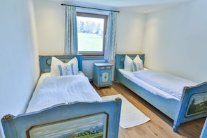 A room with two beds, a window with curtains, a radiator, and a small bedside table. - Holiday apartment with 1 bedroom (Schliersee)