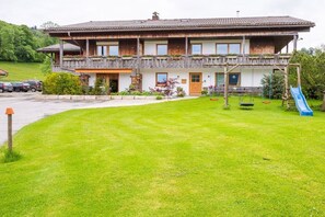 Een tweegelegen chalet met een balkon, een veranda en een kleine tuin met een schommel en een glijbaan.