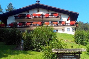 A multi-story building with balconies adorned with red flowers, a signboard, and a flag. - Bergschlössl Holiday Apartment 18 (Oberaudorf)