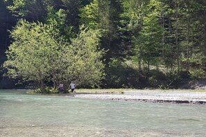 A natural setting with a riverbank, trees, and two people standing by the water. - Bergschlössl Holiday Apartment 18 (Oberaudorf)