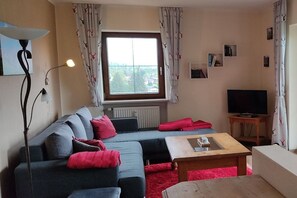A living room with a sofa, a coffee table, a TV, and a window with curtains. - Bergschlössl Holiday Apartment 18 (Oberaudorf)