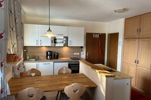 A compact kitchen with white cabinets, a microwave, a coffee maker, and a wooden dining table with heart-shaped chairs. - Bergschlössl Holiday Apartment 18 (Oberaudorf)