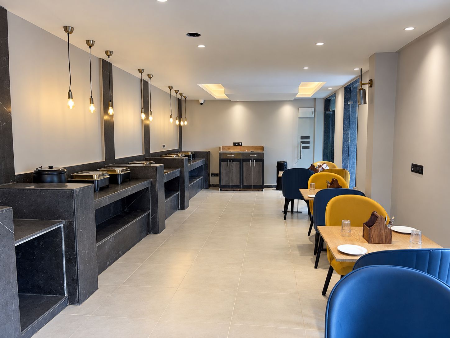 A modern restaurant with a long counter, multiple seating areas, and pendant lighting.