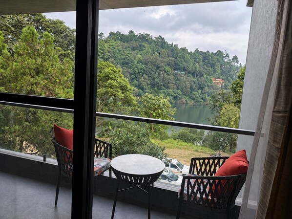 A balcony with two chairs and a small table, overlooking a lake and forested hills.