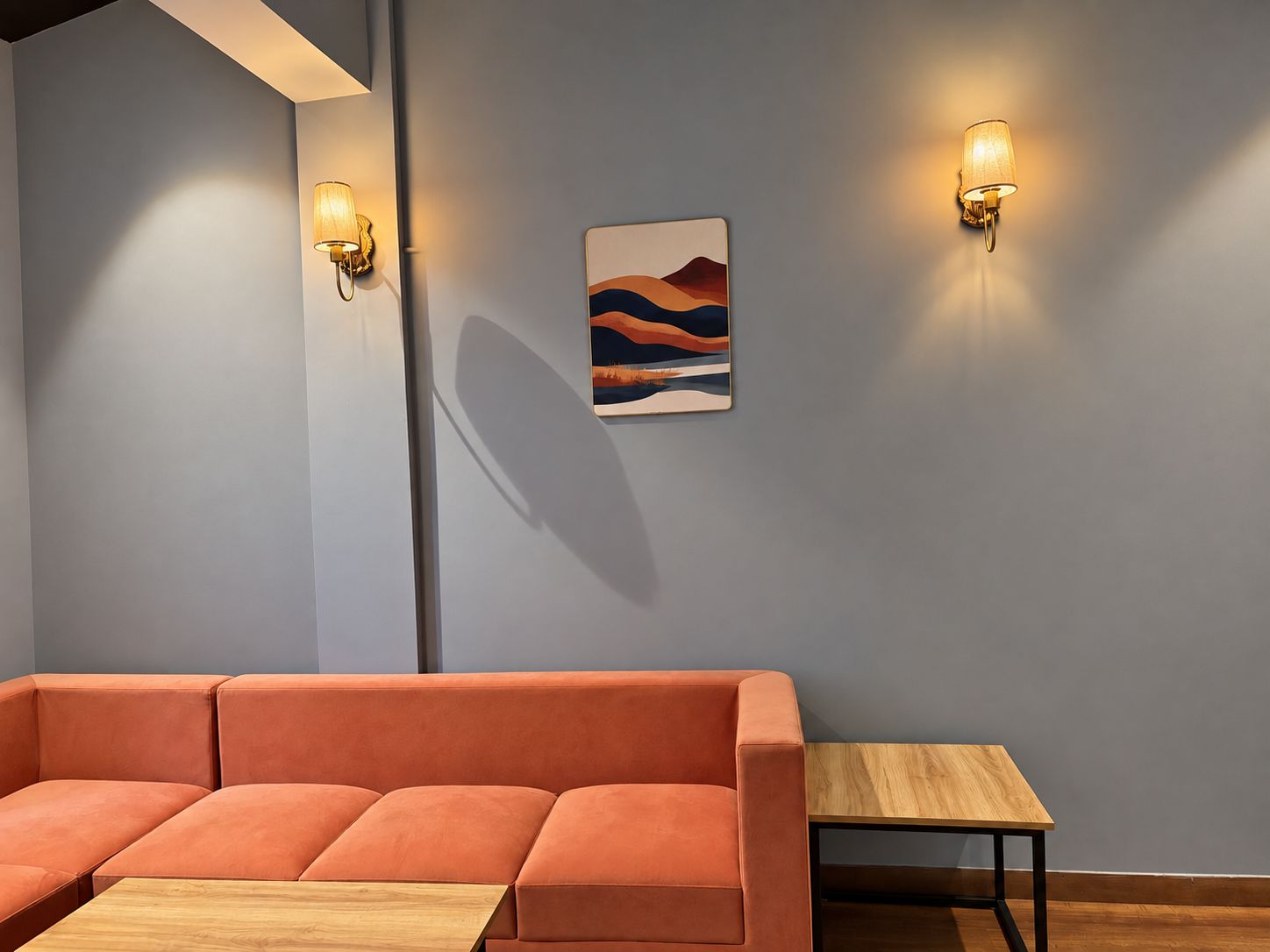 Un intérieur moderne avec un canapé d’angle, une petite table en bois et deux appliques murales.
