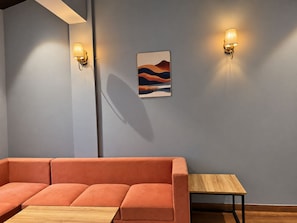 A modern interior with a sectional sofa, a small wooden table, and two wall-mounted light fixtures.