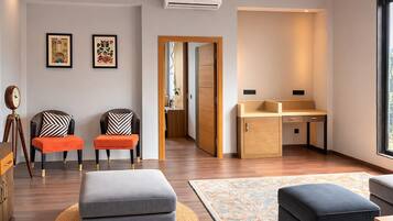 A modern living room with a sofa, ottomans, a desk, and a small kitchenette.