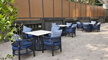 An outdoor seating area with wicker chairs and tables, a wooden fence, and a tiled floor.