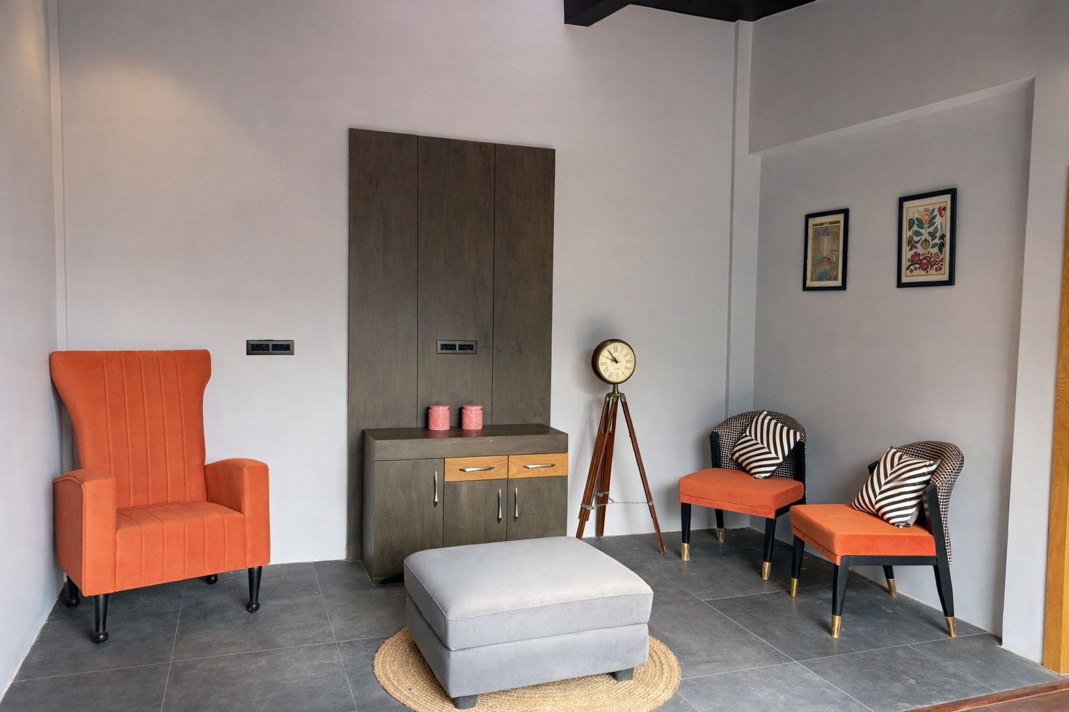 A modern living room with a large grey sofa, an orange armchair, a grey ottoman, a wooden cabinet, and a floor lamp.