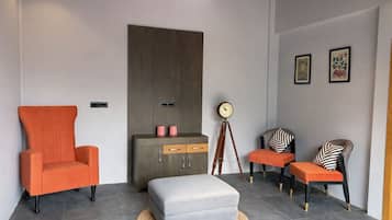 A modern living room with a large grey sofa, an orange armchair, a grey ottoman, a wooden cabinet, and a floor lamp.