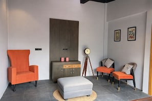 Una sala de estar moderna con un sofá gris grande, un sillón naranja, un otoman gris, un mueble de madera y una lámpara de pie.
