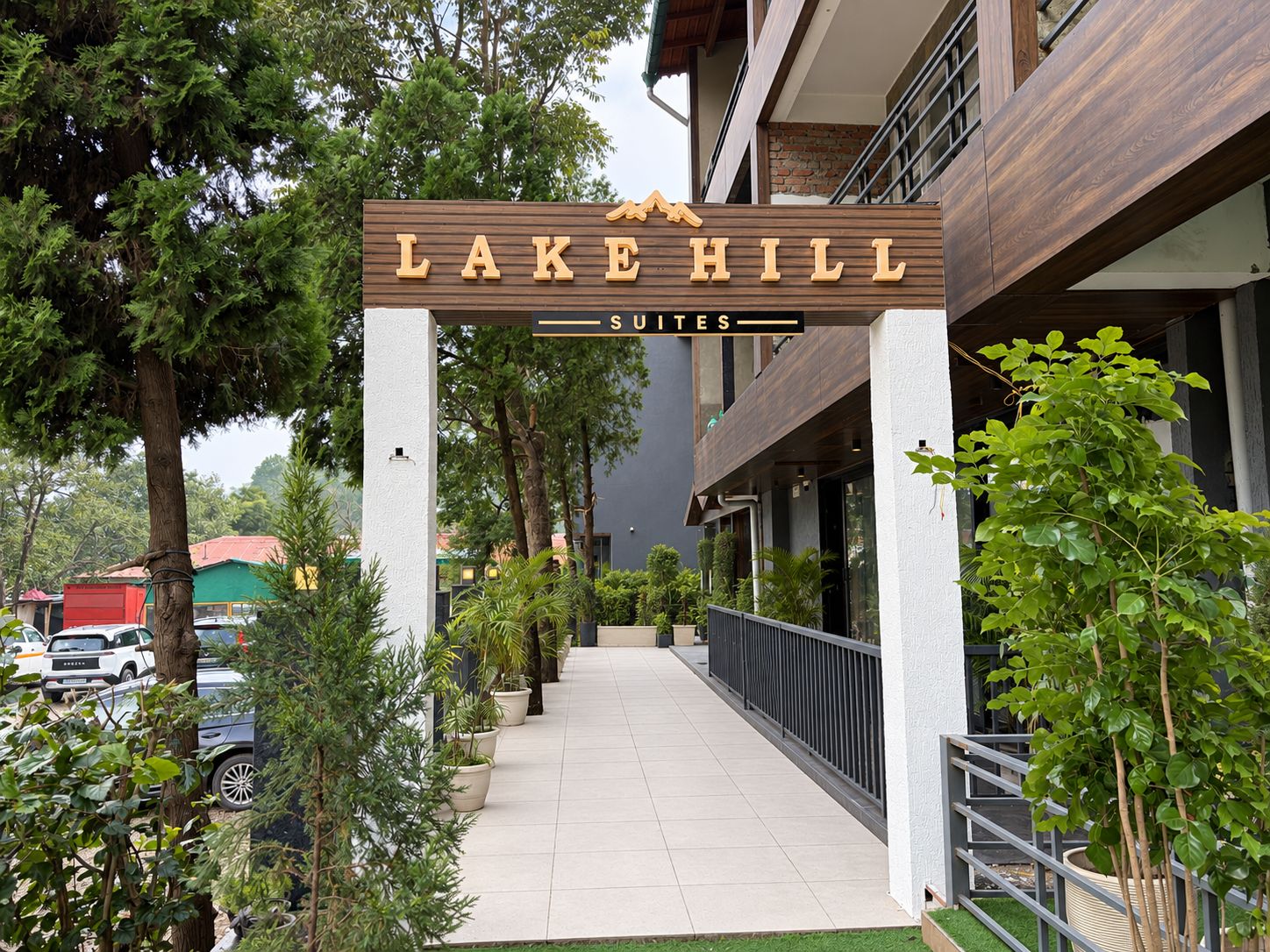 A hotel entrance with a sign reading 'LAKE HILL SUITES' and a pathway leading to the building.
