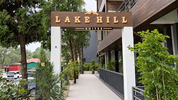 A hotel entrance with a sign reading 'LAKE HILL SUITES' and a pathway leading to the building.