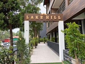 Entrada de un hotel con un letrero que dice 'LAKE HILL SUITES' y un camino que lleva al edificio.