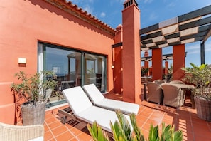 A terrace with a glass door leading to a room, two white lounge chairs, wicker furniture, and potted plants. - Bonita Hills – Penthouse in Calahonda with Panoramic Sea Views & Large Terrace (Mijas)