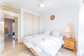 Een slaapkamer met een bed, nachtkastje, lamp en een deur naar een andere kamer.