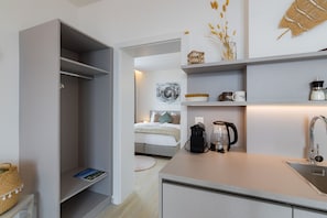 Ein kompaktes Hotelzimmer mit Küchenzeile, einem Bett mit Nachttisch und einer kleinen Sitzecke.