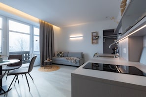 Eine moderne Küche mit Einbauherd, ein Essbereich mit rundem Tisch und Stühlen sowie eine Wohnbereich mit Sofa und Couchtisch.