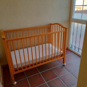 Een houten ledikant met een witte matras op een betegelde vloer, geplaatst bij een raam met uitzicht op een gebouw.