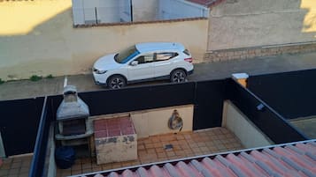 Une voiture blanche est garée dans la rue, un bâtiment avec un toit recouvert de tuiles, et une clôture noire.