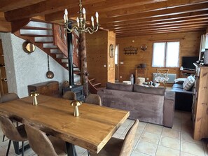A cozy cabin interior with a wooden dining table, cushioned seating, a fireplace, and a staircase. - Family chalet in the heart of the village, sleeps 8, with a garden, terrace, and direct access to the slopes (Corrençon-en-Vercors)