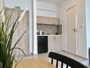 A compact kitchen with a refrigerator, a sink, and a countertop with various appliances. There is a dining table with chairs and a potted plant. - 6th Floor Loft in the Heart of Athens Ι by ΜΡS (Athina)