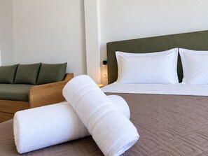 A hotel room with a bed, a green sofa, and two rolled white towels. - 6th Floor Loft in the Heart of Athens Ι by ΜΡS (Athina)