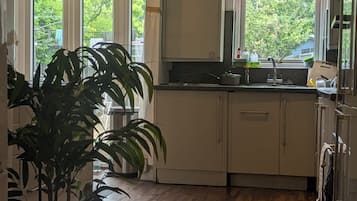 Cozinha com piso de madeira, uma planta em vaso e uma janela com cortina vermelha.