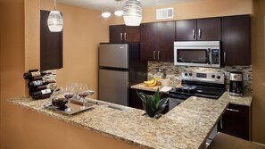Une cuisine moderne avec des meubles en bois foncé, des appareils en acier inoxydable, des plans de travail en granit et des luminaires suspendus.