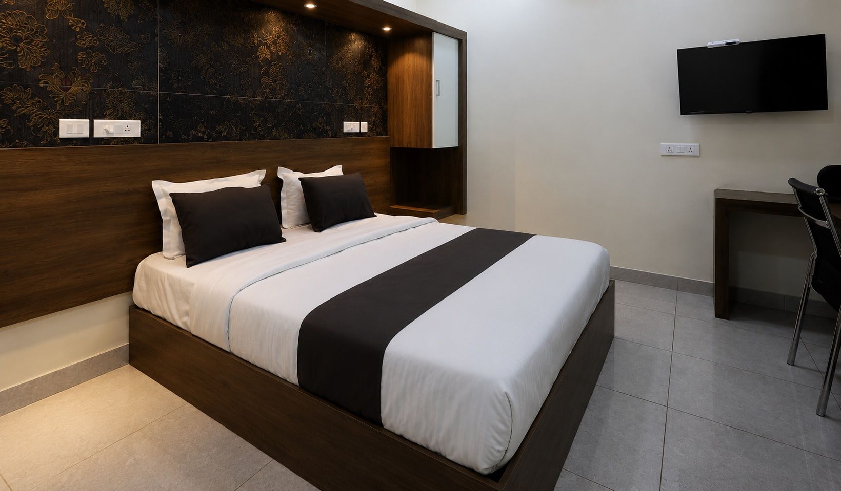 A modern hotel room with a large bed, a wooden headboard, a flat-screen TV, and a small desk area.