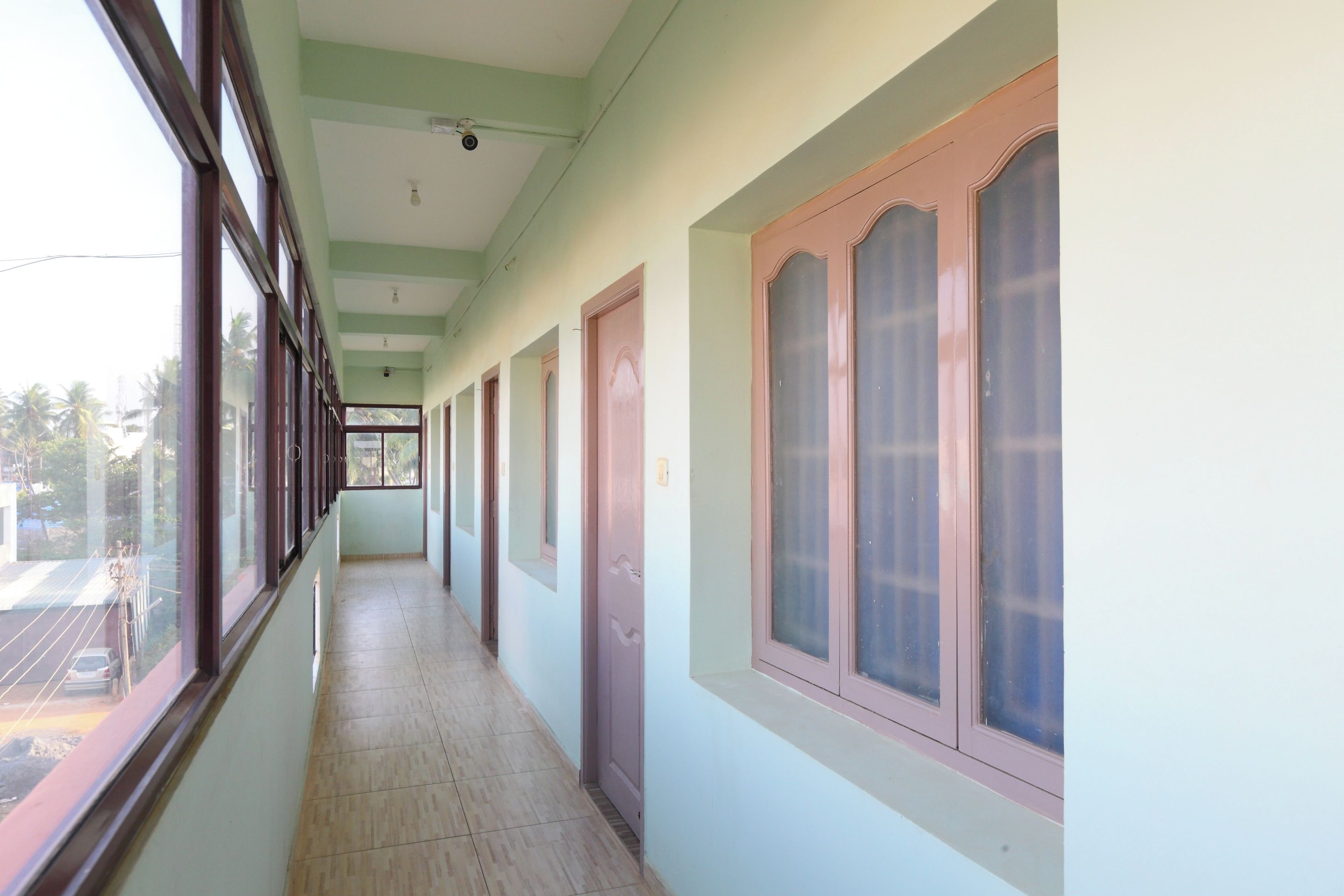 A corridor with doors and windows, leading to a room with a view of palm trees.