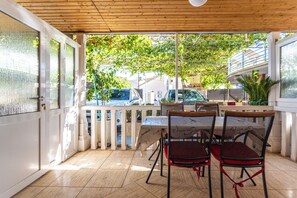 An outdoor patio with a table and chairs, a wooden ceiling, and a view of the street and trees. - A2 - Cozy apartment with pool and spacious terrace, 2 min walk to beach (Omiš)